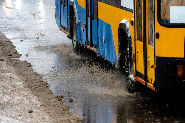 Passaggio di auto in una grande pozzanghera durante la pioggia e il nevischio Grandi schizzi da sotto le ruote dell'auto Fango, neve e pozzanghere su una delle principali autostrade della città