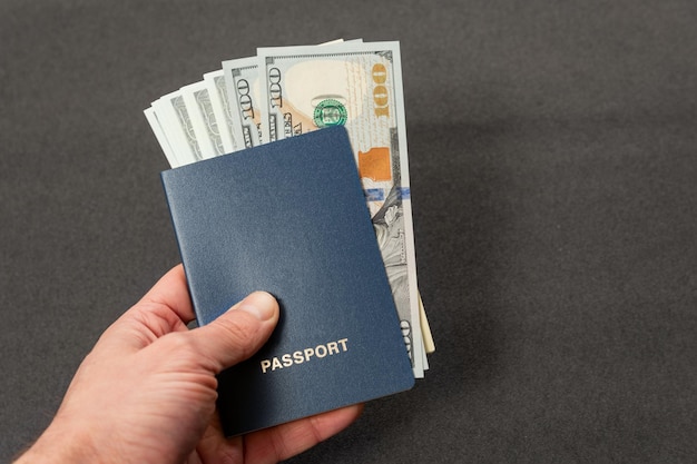 Passaporto blu con copertina vuota e dollari in contanti nella mano dell'uomo su sfondo grigio Concetto di viaggio di emigrazione o corruzione