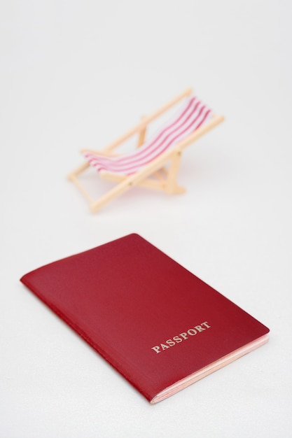 Passaporto rosso e sedia a sdraio rossa su sfondo bianco.