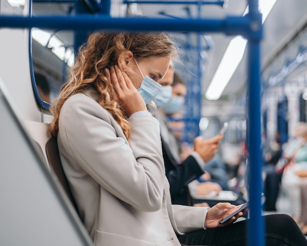 Passeggeri con maschere protettive che usano i loro gadget nel vagone della metropolitana