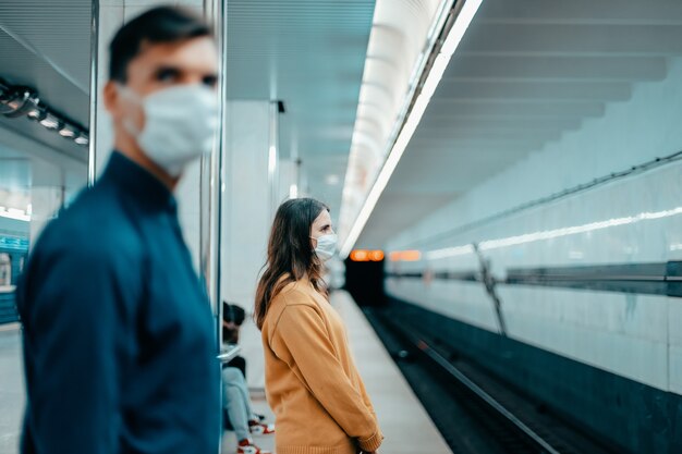 Passeggeri con maschere protettive in piedi alla stazione della metropolitana