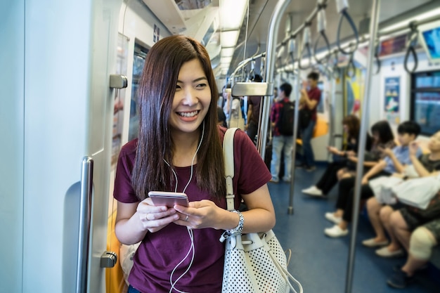 Passeggero asiatico della donna con il vestito casuale facendo uso del telefono cellulare astuto