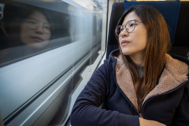 Passeggero asiatico della giovane signora che si siede in un umore depresso accanto alla finestra dentro il treno