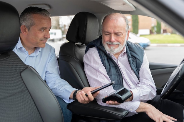 Passeggero di mezza età sul sedile posteriore che paga con l'app mobile al conducente anziano Concetto di trasporto taxi taxi e tecnologia