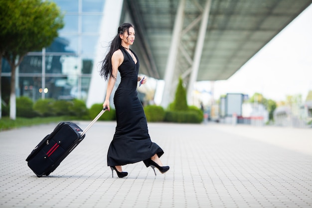 Passeggero femminile sorridente che procede tirando valigia attraverso l'aeroporto