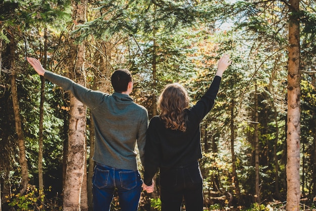 Passeggiata autunnale nella foresta. Vista posteriore della coppia in piedi con le braccia tese. L'uomo e la donna in abiti caldi sono felici.