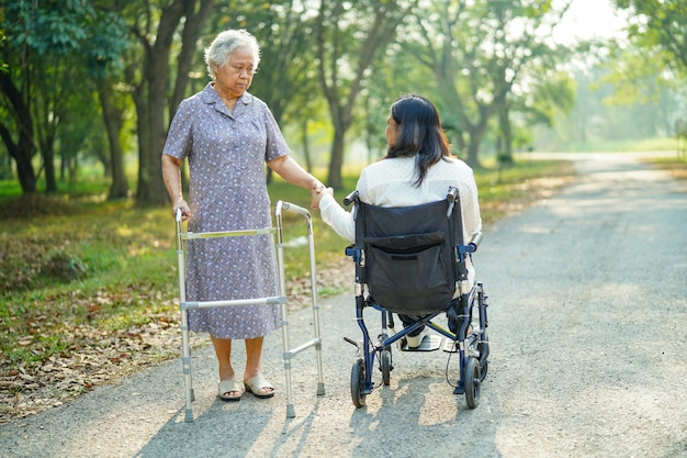 Passeggiata senior asiatica di signora con il camminatore e la donna sulla sedia a rotelle in parco.