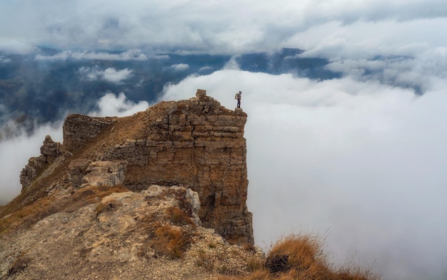 Passeggiate turistiche sulla montagna vicino al bordo dell'abisso in alta quota sotto il cielo nuvoloso in una giornata di nebbia Uomo su roccia alta vicino al bordo del precipizio con meravigliosa vista nebbiosa dall'alto alla vasta catena montuosa in lontananza