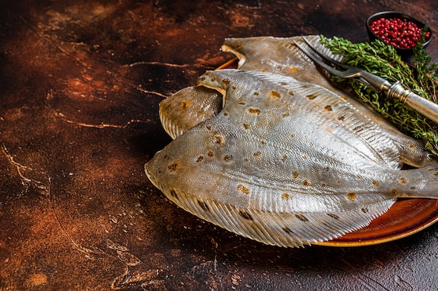 Passera cruda o passera di mare su piatto rustico con erbe aromatiche. Sfondo scuro. Vista dall'alto. Copia spazio.