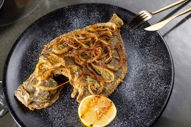 Passera fritta con cipolla e limone su un piatto di argilla nera