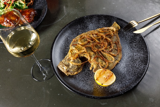 Passera fritta con cipolla e limone su un piatto di argilla nera