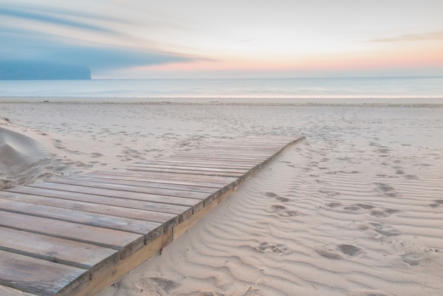 Passerella in legno che entra in spiaggia al sorgere del sole