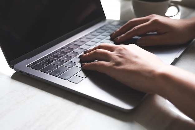 Passi la battitura a macchina sulla tastiera del computer portatile con la tazza di caffè sulla tavola