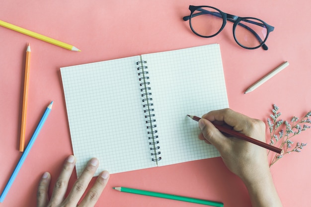 Passi la scrittura sul taccuino in bianco con le matite di colore sul fondo di colore