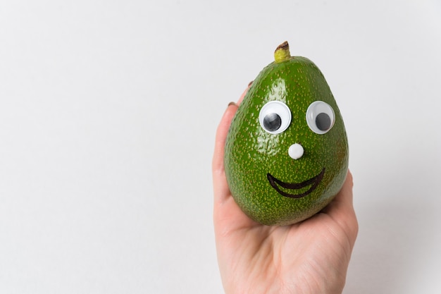 Passi la tenuta dell'avocado divertente con gli occhi googly e sorrida. Concetto di cibo sano