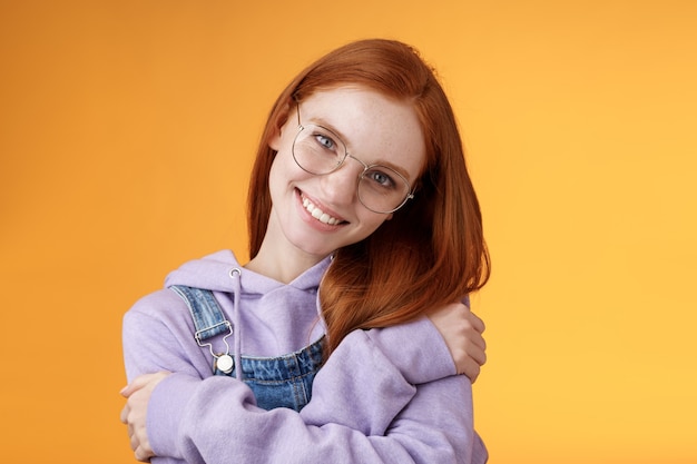 Passione, tenerezza, concetto di benessere. La ragazza accetta la propria auto sorridente affascinante sorriso inclinato la testa che si abbraccia abbracciando il corpo sentire la felicità deliziata rilassante, lo sguardo civettuolo della fotocamera sfondo arancione.