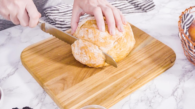 Passo dopo passo. Affettare una pagnotta di ciabatta con un coltello da pane su un tagliere di legno.