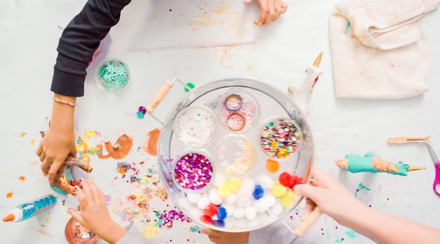 Passo dopo passo. Bambine che decorano unicorno di cartapesta con glitter e fiori di carta.