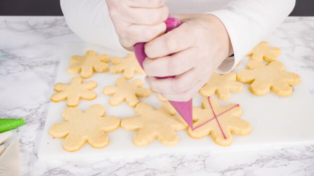 Passo dopo passo. Glassa i biscotti di zucchero a forma di fiocco di neve con glassa reale rosa.