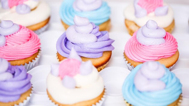 Passo dopo passo. Il pasticcere che pipa la glassa di crema al burro sui cupcakes di unicorno per la festa di compleanno della bambina.