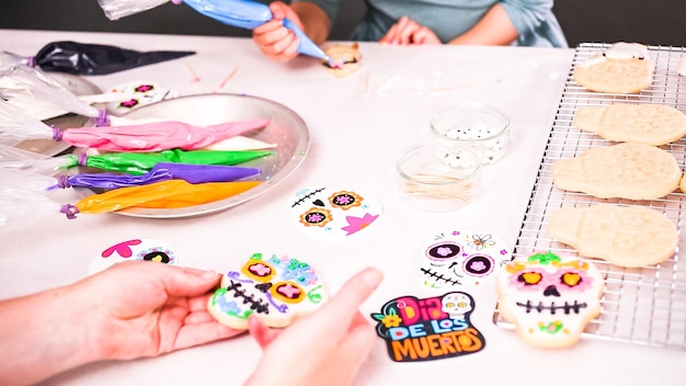 Passo dopo passo. Madre e figlia che decorano i biscotti con teschio di zucchero con glassa reale per la festa del Dia de los Muertos.