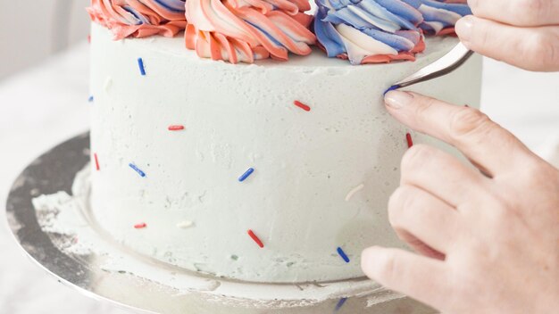 Passo dopo passo. Mettere dei granelli di colore sui lati della torta rotonda alla vaniglia a tre strati.