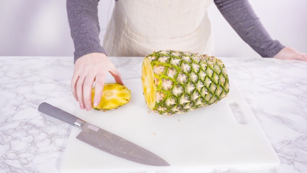 Passo dopo passo. Tagliare l'ananas su un tagliere bianco.