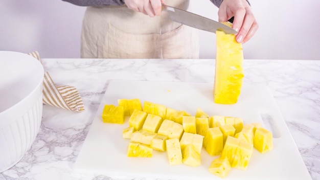 Passo dopo passo. Tagliare l'ananas su un tagliere bianco.