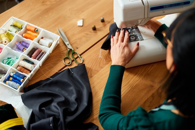 Passo dopo passo, una donna anziana di 50 anni cuce vestiti sulla macchina da cucire, sarto maturo che lavora con il cucito in atelier, industria tessile, hobby, spazio di lavoro.