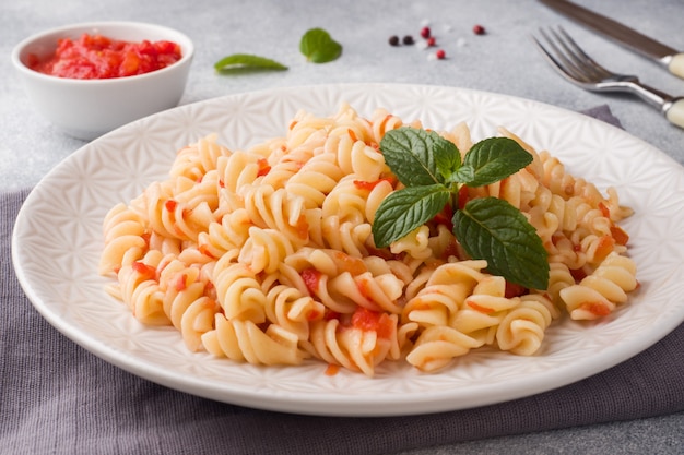 Pasta a spirale mescolata con i pomodori ciliegia e la salsa al pomodoro su un piatto.