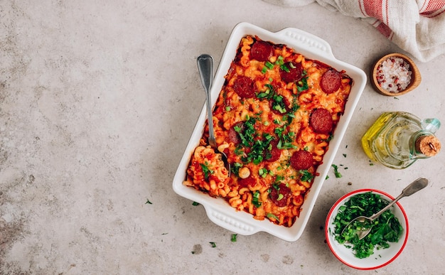 Pasta al forno in salsa di pesto di pomodoro con erbe aromatiche e peperoni Pasta per pizza piccante su fondo in cemento Vista dall'alto