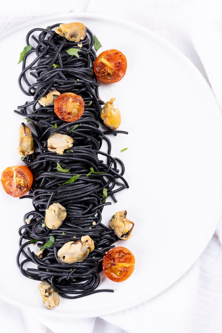 Pasta al nero di seppia con frutti di mare: cozze su un piatto bianco su fondo di legno bianco