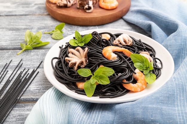 Pasta al nero di seppia con gamberi o gamberi e polpi su fondo di legno grigio e tessuto blu. Vista laterale,