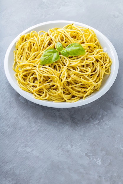 Pasta al pesto di salsa e foglie di basilico su un piatto bianco