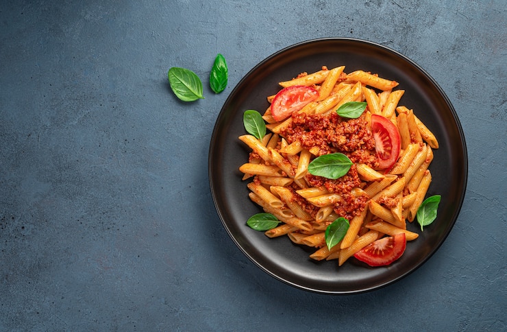 Foto pasta al ragù alla bolognese, basilico fresco e pomodori in lastra nera su fondo grafite. vista dall'alto, orizzontale.