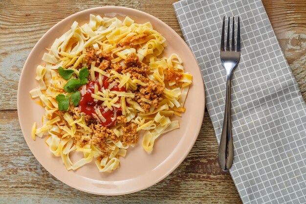 Pasta alla bolognese al pomodoro guarnita con erbe aromatiche e formaggio in un piatto su un tavolo di legno