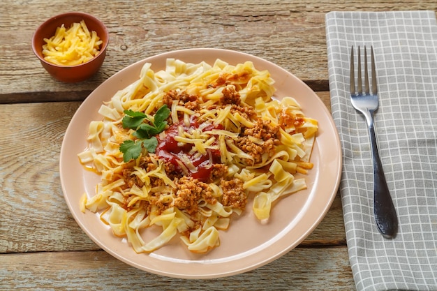 Pasta alla bolognese al pomodoro guarnita con erbe e formaggio in un piatto su un tavolo di legno accanto a una forchetta e tovagliolo e formaggio grattugiato in un piatto Foto orizzontale