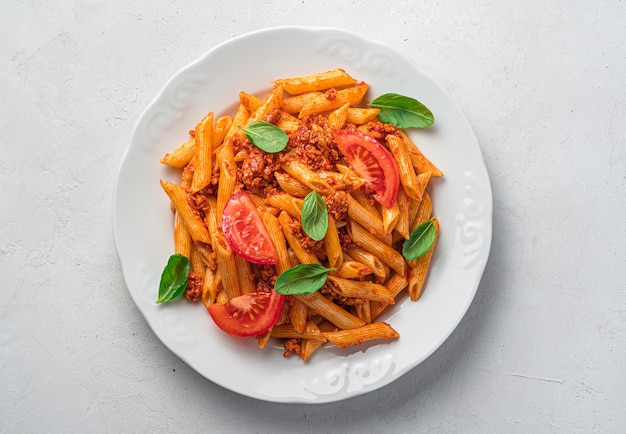 Pasta alla bolognese con basilico e pomodori freschi su sfondo grigio. Un piatto della tradizione italiana. Vista dall'alto, primo piano.