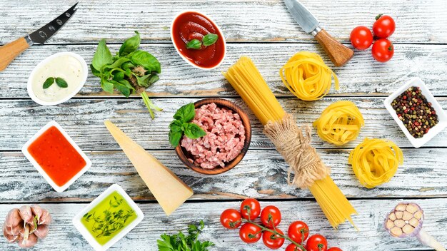 Pasta alla bolognese e ingredienti su fondo di legno bianco Vista dall'alto Spazio libero per il testo