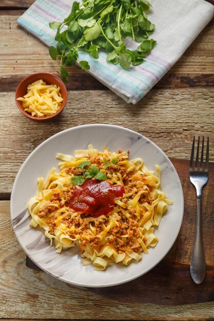 Pasta alla bolognese guarnita con verdure e formaggio in un piatto su un tavolo di legno su una tavola lucida