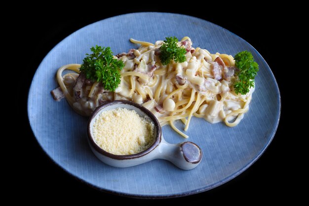 Pasta alla carbonara con pancetta su piatto blu isolato su sfondo nero vista laterale