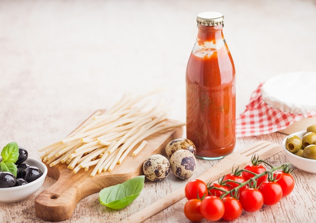 Pasta casalinga organica fresca degli spaghetti con le uova di quaglia e pomodori freschi con la bottiglia di salsa al pomodoro e spatola di legno e foglia del basilico. Cibo italiano classico