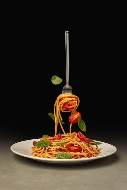 Pasta che cade in un piatto con pomodoro e basilico su sfondo nero Levitazione