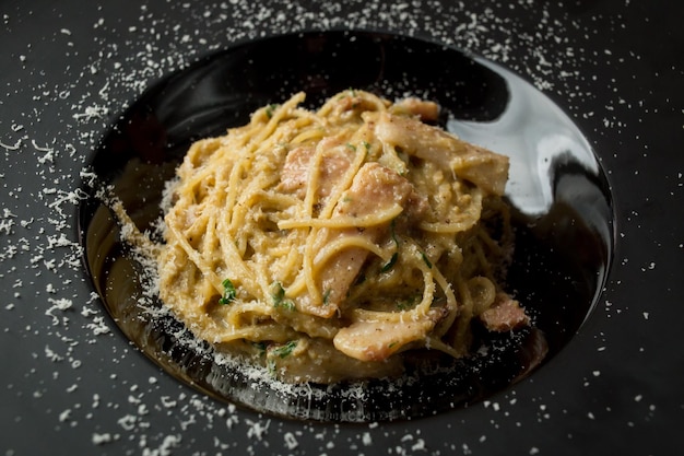 Pasta con fette di prosciutto parmigiano alle erbe e uovo su un piatto nero su fondo di legno