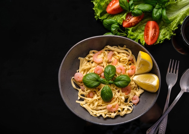 Pasta con gamberetti, basilico e pomodori su uno sfondo scuro. Vista dall'alto