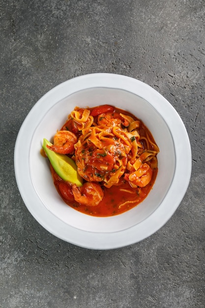 Pasta con gamberetti e salsa di pomodoro in piatto bianco su sfondo di cemento copia spazio