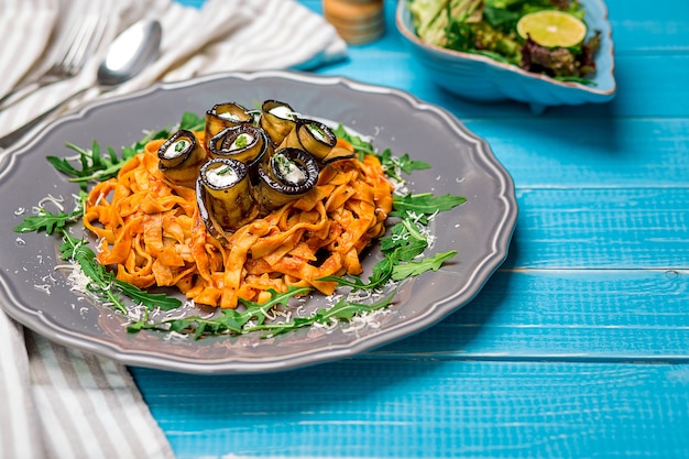 Pasta con melanzane, pomodoro, formaggio e rucola. La presentazione originale del piatto da parte dello chef. Su uno sfondo di legno blu.