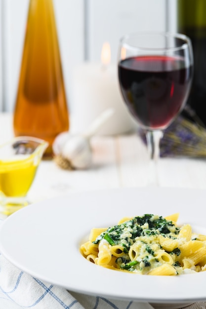 Pasta con mozzarella spinaci e vino su sfondo chiaro.