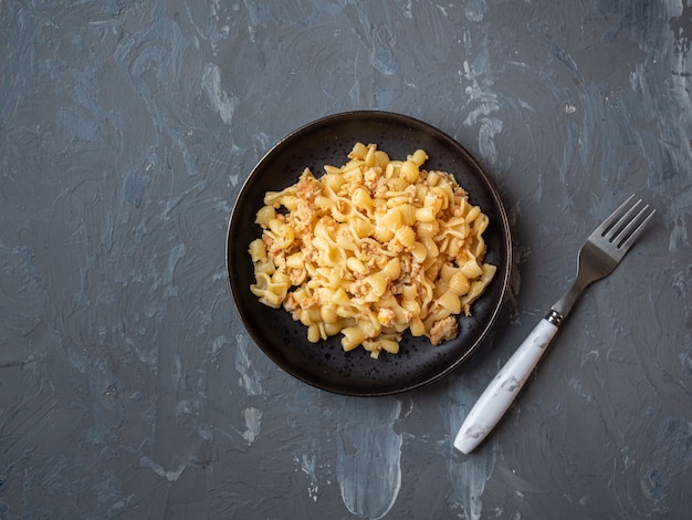 Pasta con pollo tritato che serve su un piatto rotondo nero e forchetta su fondo nero flatlay