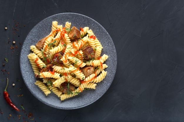 Pasta con pomodori, pollo e prezzemolo su un piatto su un tavolo scuro. Foto Premium.